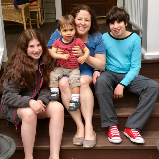Ellen Seidman, author of Love That Max with her children. From left to right: a young woman, a baby boy, Ellen herself, and a young man with cerebral palsy sit on a stoop.